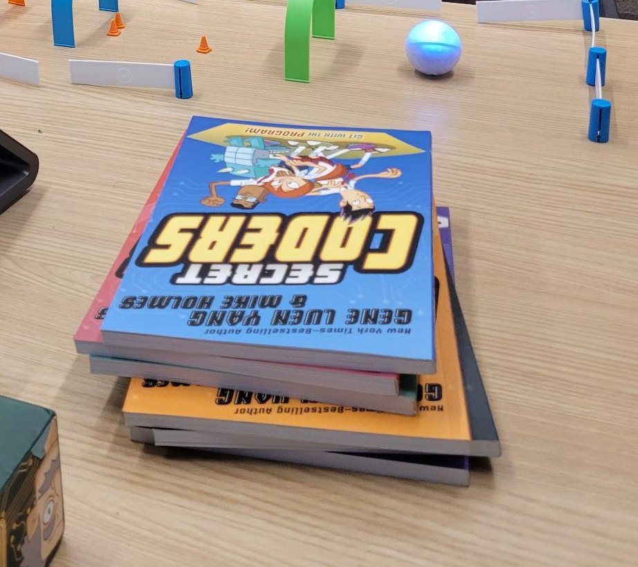 Secret Coders books stacked on the table beside the small blue robot.