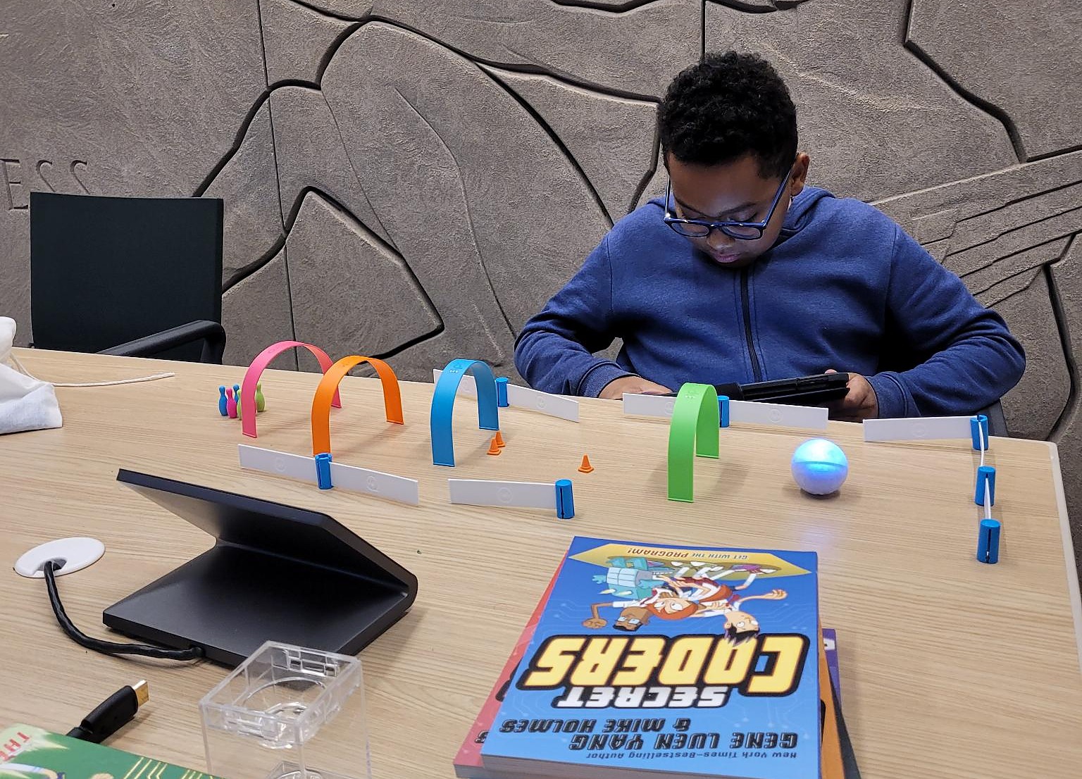 A boy at a table programming a small rolling robot through a course of coloured arches.
